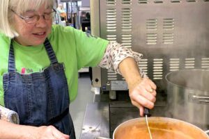 Older woman in kitchen with pot of food