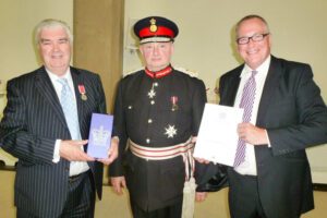 Two men in suits and one in army uniform receiving award