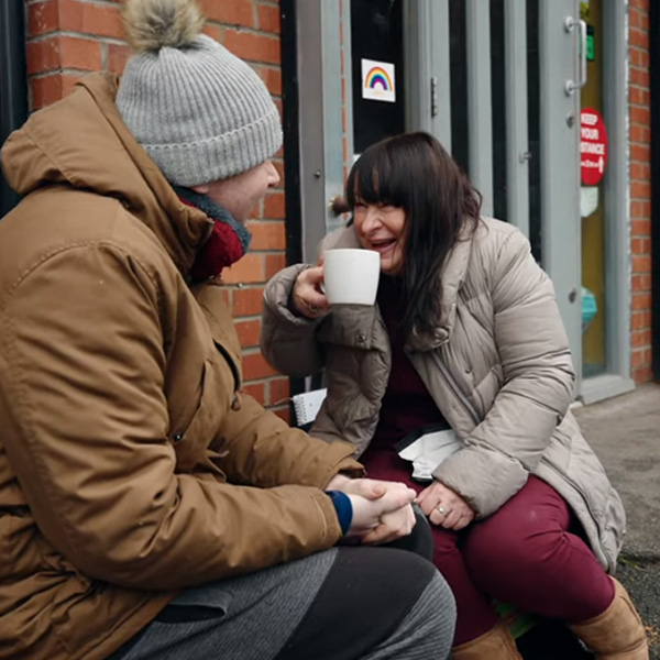 Woman speaking to man outside laughing with mug